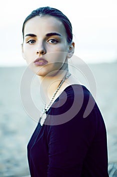 young pretty brunette girl with long hair waiting alone on sand at seacoast, lifestyle people concept