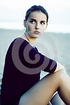 Young pretty brunette girl with long hair waiting alone on sand at seacoast, lifestyle people concept