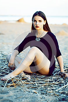 Young pretty brunette girl with long hair waiting alone on sand at seacoast, lifestyle people concept