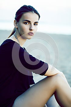 Young pretty brunette girl with long hair waiting alone on sand at seacoast, lifestyle people concept