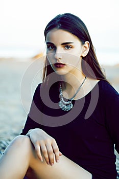 Young pretty brunette girl with long hair waiting alone on sand at seacoast, lifestyle people concept