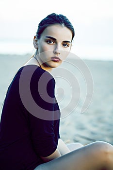 Young pretty brunette girl with long hair waiting alone on sand at seacoast, lifestyle people concept