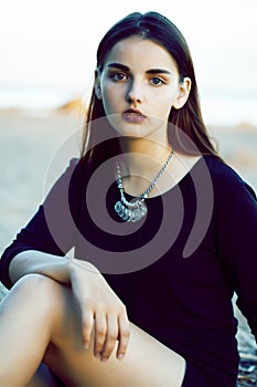 Young pretty brunette girl with long hair waiting alone on sand at seacoast, lifestyle people concept