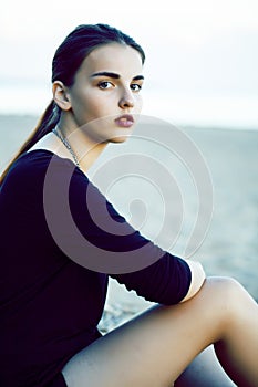 Young pretty brunette girl with long hair waiting alone on sand at seacoast, lifestyle people concept