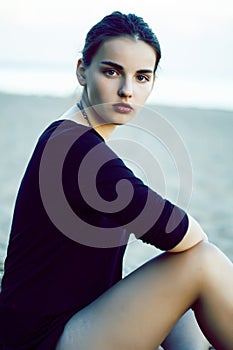 Young pretty brunette girl with long hair waiting alone on sand at seacoast, lifestyle people concept