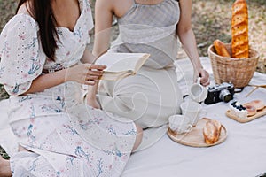 Young pretty brunette twin girls sitting on the grass with legs slightly bent in knees and looking in a brown book, wearing casual