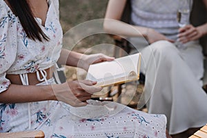 Young pretty brunette twin girls sitting on the grass with legs slightly bent in knees and looking in a brown book, wearing casual