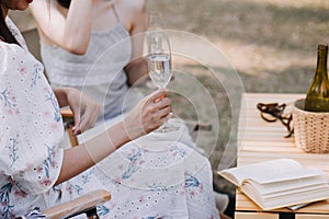 Young pretty brunette twin girls sitting on the grass with legs slightly bent in knees and looking in a brown book, wearing casual