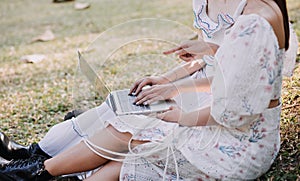 Young pretty brunette twin girls sitting on the grass with legs slightly bent in knees and looking in a brown book, wearing casual