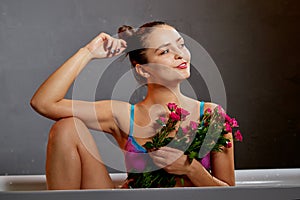 Young pretty brunette woman in bath with water and flowers in a dark room