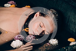 Young pretty brunette woman in bath with water and flowers. Naked model during an unusual photo shoot in a black bath