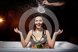 Young pretty brunette woman in bath with water and splashes and drops in a dark room