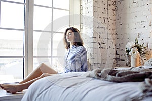 Young pretty brunette woman in her bedroom sitting at window, happy smiling lifestyle people concept