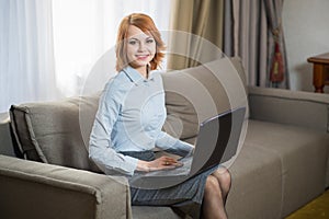 Young pretty business woman with laptop sitting on couch in the hotel room