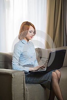 Young pretty business woman with laptop sitting on couch in the hotel room