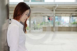 Young pretty business woman leaning a pole and thinking something in public outdoor with copy space background.