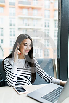 Young pretty businesswoman sitting in cafe in front of laptop and networking talking via headphones