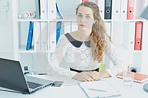 Young pretty businesswoman sitting at office desk, smiling.