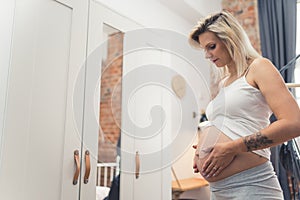 young and pretty Caucasian pregnant woman touching her belly and caring about her health, pregnancy concept