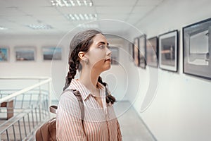 Young pretty caucasian thoughtful woman watching at the artwork. Side view. Exhibition in the art gallery. Excursion and