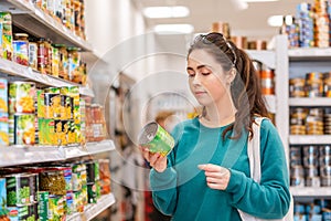 A young pretty Caucasian woman reads ingredients on a tin of canned peas. The concept of buying products and shopping