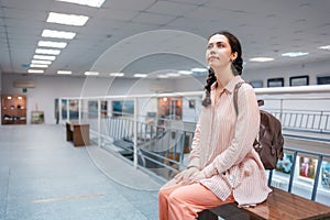 Young pretty caucasian woman sitting on bench contemplating at the artwork. Exhibition in the art gallery. Excursion and