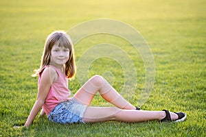 Young pretty child girl laying down on green grass lawn on warm summer day
