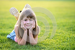 Young pretty child girl laying down on green grass lawn on warm summer day