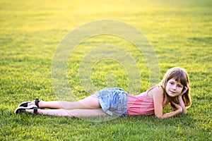 Young pretty child girl laying down on green grass lawn on warm summer day