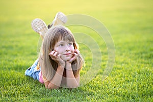 Young pretty child girl laying down on green grass lawn on warm summer day