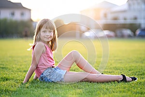 Young pretty child girl laying down on green grass lawn on warm summer day