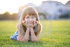 Young pretty child girl laying down on green grass lawn on warm summer day