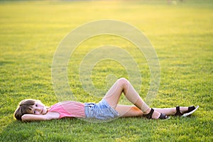 Young pretty child girl laying down on green grass lawn on warm summer day