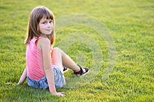 Young pretty child girl laying down on green grass lawn on warm summer day