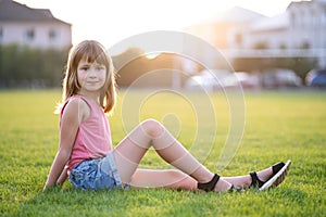 Young pretty child girl laying down on green grass lawn on warm summer day