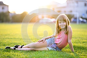 Young pretty child girl laying down on green grass lawn on warm summer day