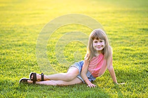 Young pretty child girl laying down on green grass lawn on warm summer day