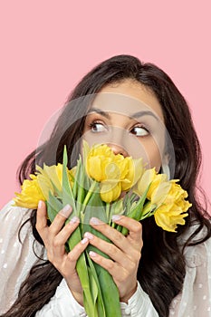 Young pretty dark-haired woman holding yellow flowers and looking surprised