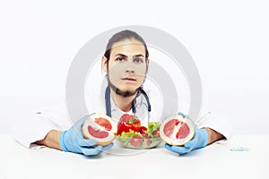 Young pretty doctor with stethoscope holding fruits, vegetables and pills, syringe, healthy food care concept