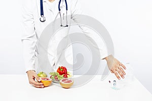 Young pretty doctor with stethoscope holding fruits, vegetables and pills, syringe, healthy food care concept