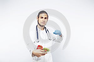 Young pretty doctor with stethoscope holding fruits, vegetables and pills, syringe, healthy food care concept
