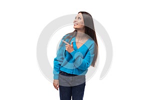young pretty european brunette woman dressed in a blue cardigan points her fingers at the advertising space