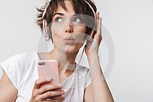 Young pretty excited happy woman posing isolated over white wall background using mobile phone listening music with earphones