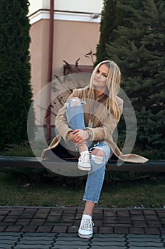 Young pretty fashionable blonde woman dressed in ripped jeans and white sweater