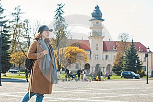 young pretty fashionable woman walking in brown coat by street