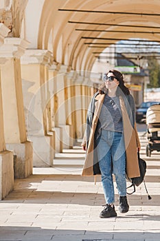 young pretty fashionable woman walking in brown coat by street