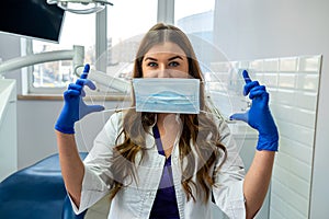 Young pretty female dentist stomatology in uniform and gloves at workplace cabinet