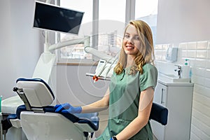 Young pretty female dentist stomatology in uniform and gloves at workplace cabinet