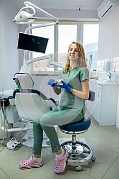 Young pretty female dentist stomatology in uniform and gloves at workplace cabinet