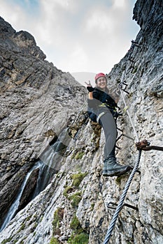 Young pretty female mountain climber on a Via Ferrata in the Dolomites in Alta Badia making a peace sign